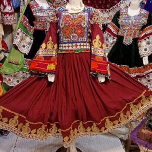 “Maroon Afghan ceremonial dress displayed on a mannequin, featuring intricate gold embroidery, colorful tribal motifs on the bodice and sleeves, and traditional mirror work. Surrounded by other vibrant handcrafted Afghan dresses.”