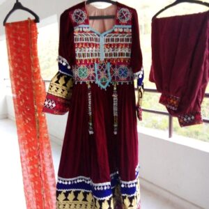 Velvet Afghani Dress for Cultural Celebrations displayed on hangers, featuring a richly embroidered maroon outfit with intricate patterns, an orange floral scarf, and matching velvet pants—showcasing traditional Afghan craftsmanship and festive elegance.