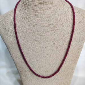 The Red Spark Ruby Necklace, featuring uniformly polished deep red beads, is elegantly displayed on a textured beige mannequin bust. Each bead reflects the vivid crimson glow of natural ruby, forming a graceful and refined design that highlights the timeless allure of the Red Spark Ruby Necklace.