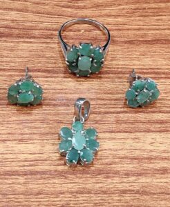 Emerald jewelry set displayed on a wooden surface, featuring a floral design with vibrant green gemstones set in 925 Rhodium Silver. Includes an adjustable ring (sizes 16–19), earrings, and pendant, arranged symmetrically to highlight artisan craftsmanship and cohesive elegance.