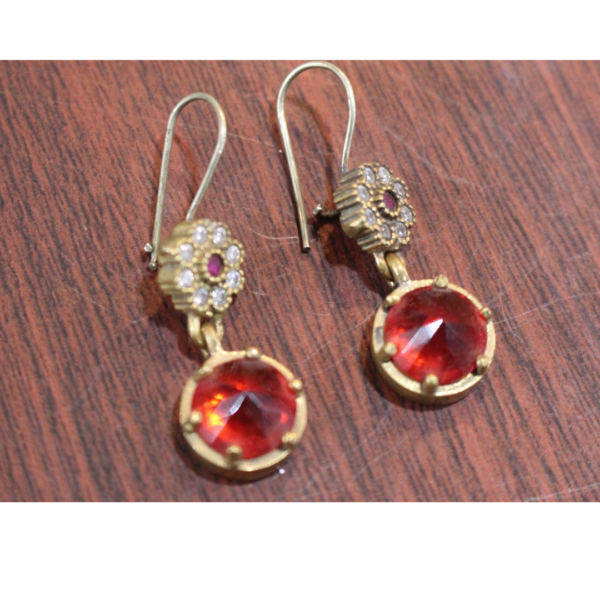 A pair of Handcrafted Red Zircon Jewelry earrings featuring round red gemstones with gold-tone settings and a floral design made of white stones, elegantly arranged on a wooden surface to highlight their intricate Afghan-inspired craftsmanship.