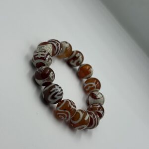 Close-up of a natural Sulimani agate bracelet showing polished beads with intricate layered patterns in earthy tones of white, grey, chocolate brown, and black, tied with