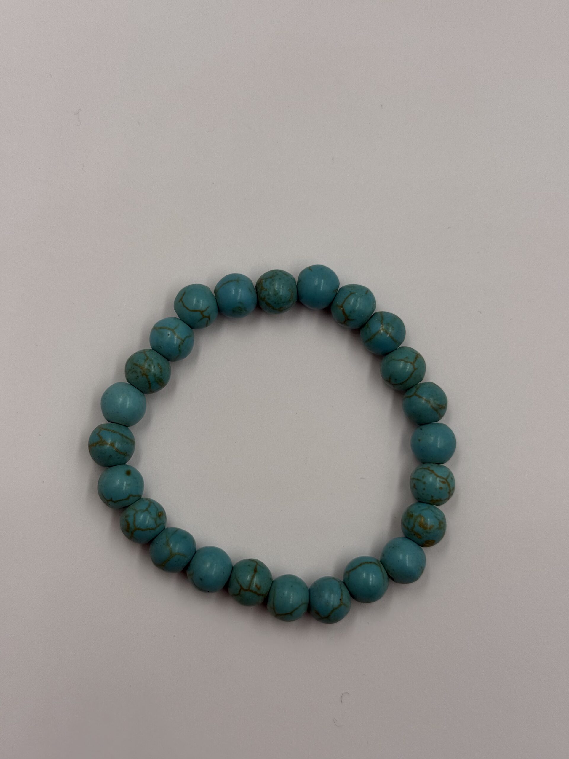 Close-up of a blue agate stone bracelet featuring various shades of blue and white banding on each bead, strung on an elastic cord with an adjustable leather closure.