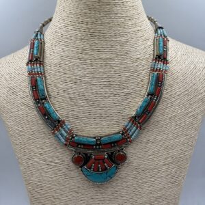 Close-up of an artisan-crafted necklace from Nepal, showcasing a raw-cut blue turquoise stone set in a polished brass pendant with silver filigree details (5% silver), on a linked chain.