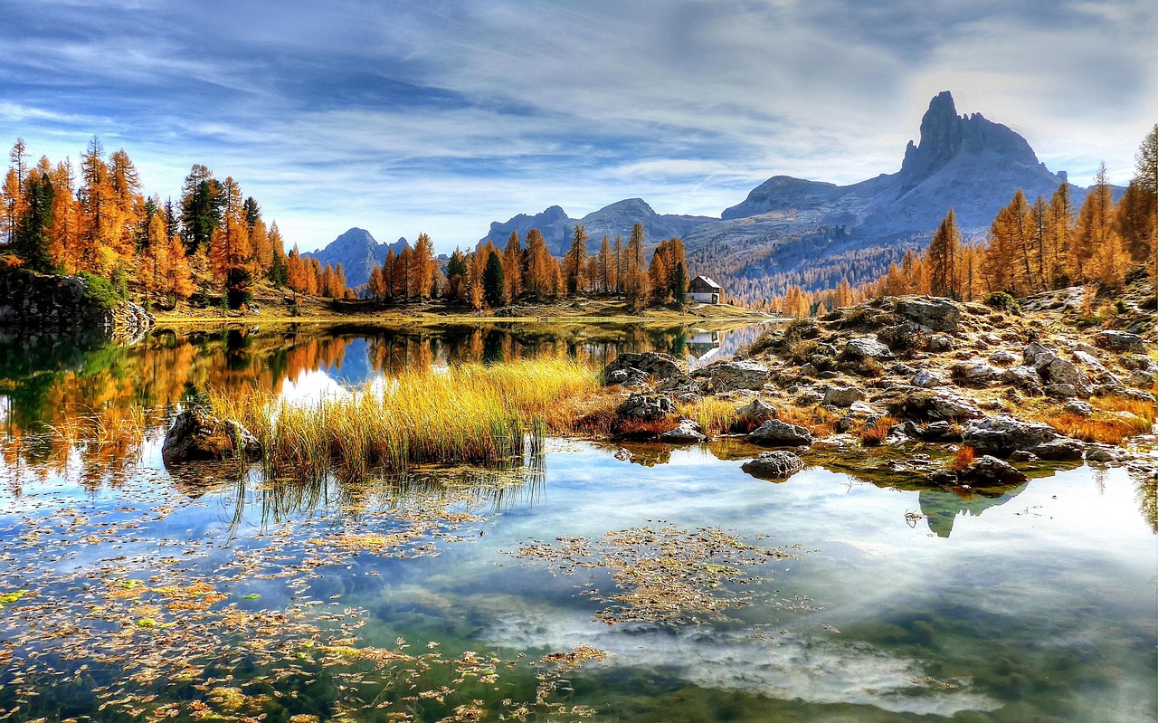 A tranquil lake surrounded by autumn-colored trees and rugged mountains, reflecting the sky and silence—symbolizing emotional clarity, sacred pause, and the quiet strength of restraint.