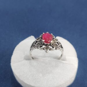 "Ornate silver ring with a central red gemstone, displayed on a white cushion against a blue fabric background, featuring floral detailing and vintage Afghan craftsmanship."
