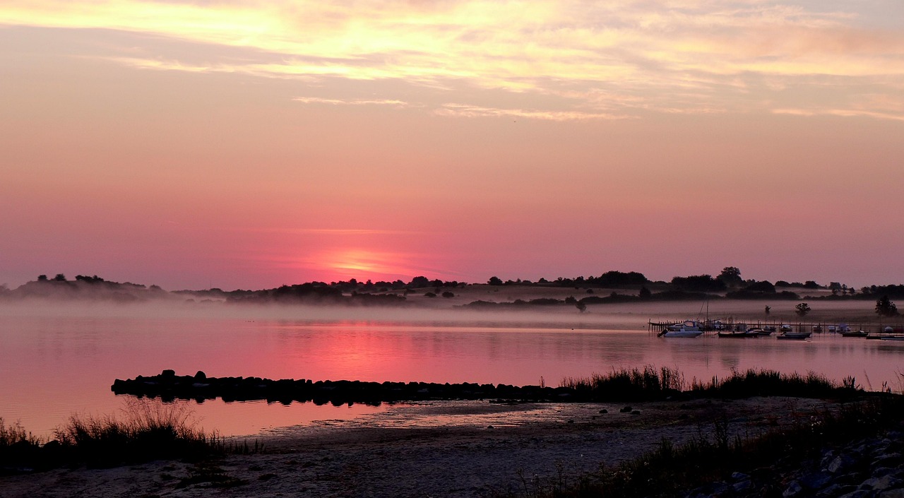 A tranquil lakeside at sunrise, with mist hovering over still waters and boats docked in quiet reflection—symbolizing the COURAGE to remain calm, walk away with dignity, and embrace silence without explanation.